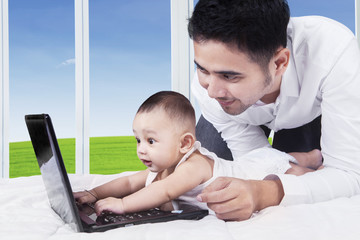 Wall Mural - Cheerful baby typing on laptop with dad