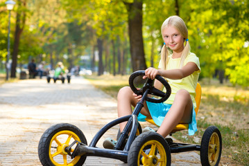 beautiful smiling little girl riding toy car in summer city park