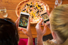 Female Friends Using Smartphones To Take Photos Of Their Pizza