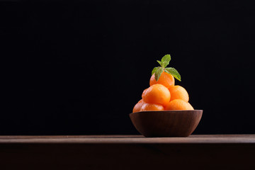 Organic cantaloupe melon in wooden bowl isolated on black backgr