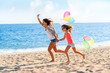 © karelnoppe - Young girls running with balloons on beach.