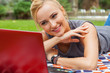 Sensual blonde woman lying in park on blanket. She is using red laptop.
