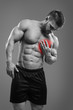 © kegfire - Muscular shirtless man with chest pain over gray background. Concept with highlighted glowing red spot.