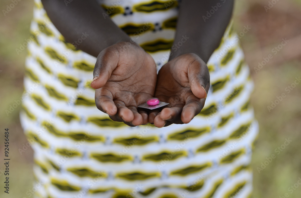 Malaria Curing Symbol African Girl Holding Pill to Cure. In Africa there are lots of diseases like malaria, pneumonia, AIDS or simple Diarrhoea. Medicine pills are important in the black continent. - obrazy, fototapety, plakaty 