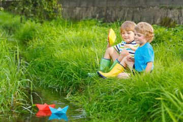 Wall Mural - Two little brothers playing with paper boats by a river