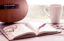 Pen On Open Notebook On Guitar And Coffee Cup In Rainy Day