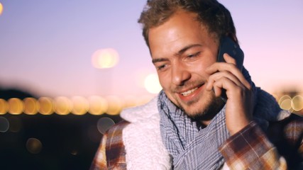 Wall Mural - Handsome young man speaking on smart phone at sunset in city