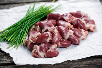 Raw Duck hearts on crumpled paper, decorated with Chives. on old wooden table