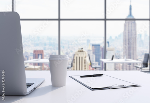 Plakat Miejsce pracy w nowoczesnym biurze panoramicznym na Manhattanie w Nowym Jorku. Na białym stole leży laptop, notatnik i filiżanka kawy. Renderowanie 3D.