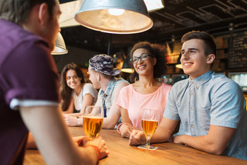 happy friends drinking beer and talking at bar