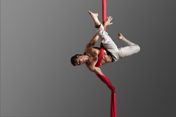 Sporty young man doing exercise with elastics, aerial silk ribbons, aerial. Sport training gym and lifestyle concept. Anti-gravity yoga.