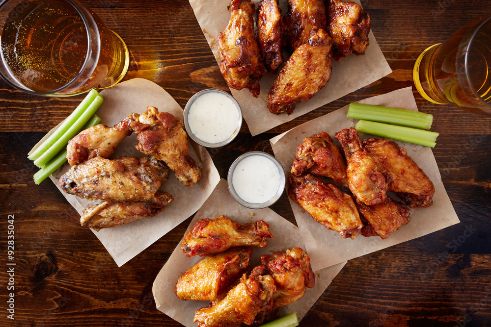 overhead view of four different flavored chicken wings with ranch dressing, beer, and celery sticks - obrazy, fototapety, plakaty 