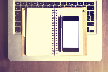 Blank smartphone, blank diary with pen and laptop on a wooden ta