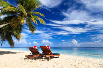 Wall Mural - two chair lounges with red Santa hats on beach