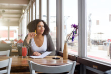 Female Student Sitting At Cafe Looking Out Of Window Daydreaming