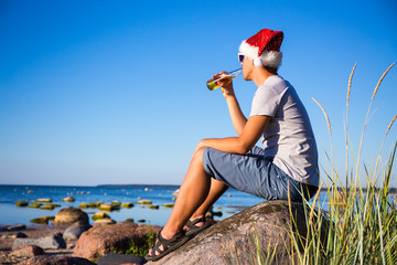 christmas concept - handsome man in santa hat drinking beer on t