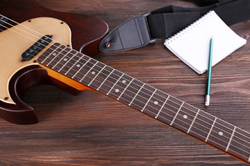 Electric guitar with notebook on wooden table close up