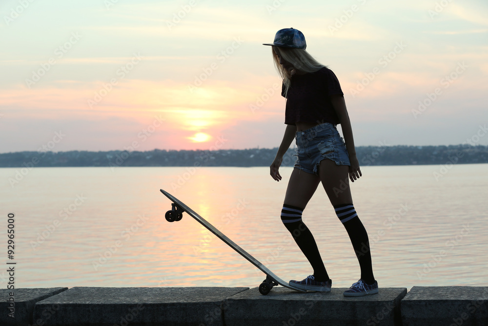 Young woman with skating board on the riverside