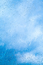 Drops Of Rain On Blue Glass Background. The Sky With Clouds On Background.