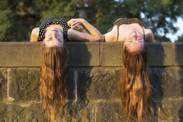 Two young girls lying on a stone slab with long hair hanging down. Beautiful soft light at sunset..