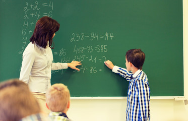 schoolboy with math teacher writing on chalk board