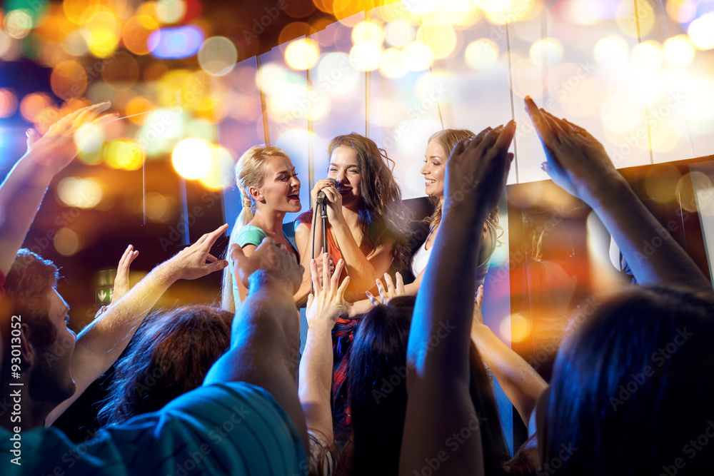 happy young women singing karaoke in night club - obrazy, fototapety, plakaty 