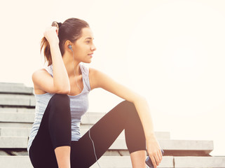 Young woman taking a break from exercising outside with cellphone, sitting