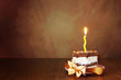 Piece of birthday chocolate cake with one burning candle against brown background