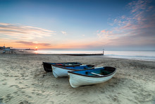 Stunning Sunrise Over A Row Of Fishing Boats On Bournemouth Beach In Dorset, With The Pier In The Far Distance
