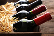 © Africa Studio - Box with straw and wine bottles on wooden background