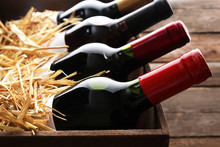 Box With Straw And Wine Bottles On Wooden Background