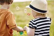 Back View Of Two Little Children Blowing Soap Bubbles