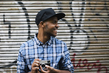 Young Man With Baseball Cap And Camera In Front Of Roller Shutter