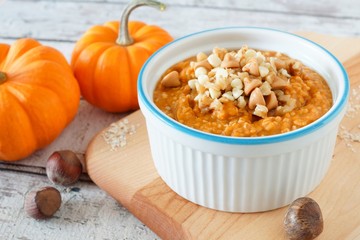 Wall Mural - bowl of autumn pumpkin oatmeal with walnuts, chocolate and peanut butter chips on wooden background