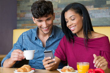 Wall Mural - Young couple looking at smartphone during breakfast