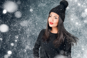 Beautiful asian woman wearing knitted hat with pompom in a snow.