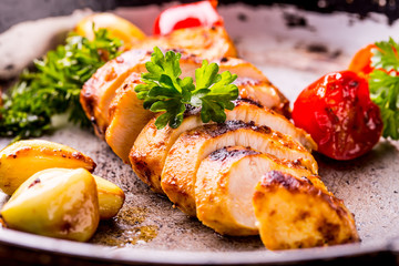 Grilled chicken breast in different variations with cherry tomatoes, green French beans, garlic, herbs, cut lemon on a wooden board or teflon pan. Traditional cuisine. Grill kitchen. 