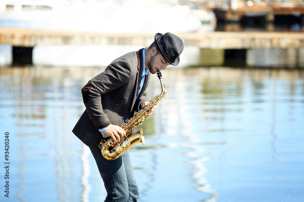 Young man playing on saxophone on the riverside