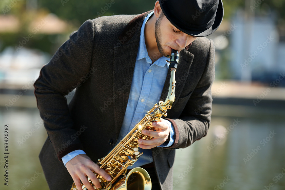 Young man playing on saxophone on the riverside