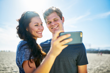Wall Mural - happy couple taking selfie on beach during sunny day with lens flare