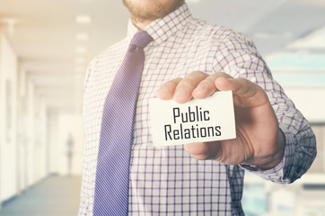 businessman in office showing card with text: Public Relations