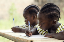 African Children At School Doing Homework. African Ethnicity Students Writing Their Essay In An African School. They're Holding Blue Pens To Write Down Their Homework Whilst Sitting In Their Desk.