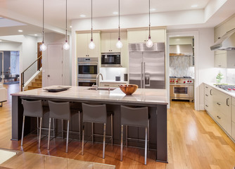 kitchen interior in new luxury home with island, stainless steel appliances, pendant lights, and cab
