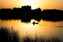 Silhouette Of A Fisherman On A Background Of City Sunset