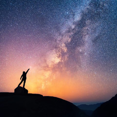 Wall Mural - catch the star. a person is standing next to the milky way galaxy pointing on a bright star.