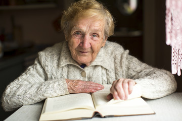 An old woman sitting with a book at the table.