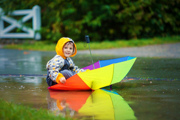 Sticker - Cute boy with colorful rainbow umbrella on a rainy day, having f