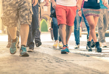 Crowd Of People Walking On The Street - Detail Of Legs And Shoes Moving On Sidewalk In City Center - Travellers With Multicolor Clothes On Vintage Filter - Shallow Depth Of Field With Sunflare Halo