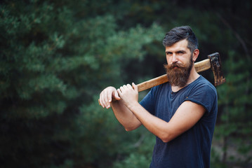 Wall Mural - brutal brunette bearded man with a hatchet in the woods on a background of trees