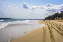 Four Wheel Drive Tracks On Sandy Beach With Boats And Vehicle In Distance. Fraser Island, Queensland, Australia.